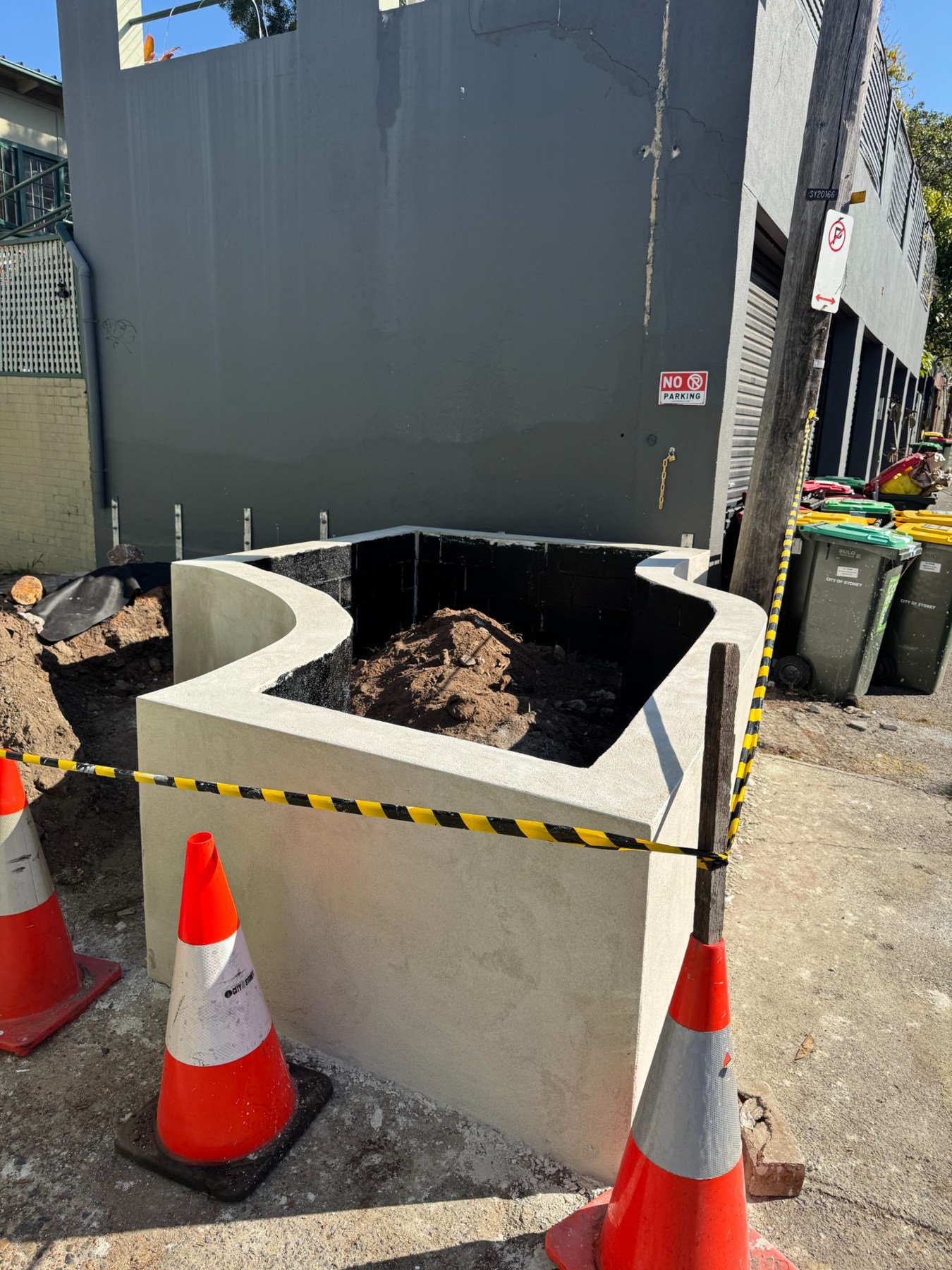A curved rendered masonry planter under construction, with black internal waterproofing